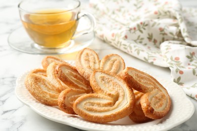 Photo of Delicious palmier cookies with tea on white marble table, closeup