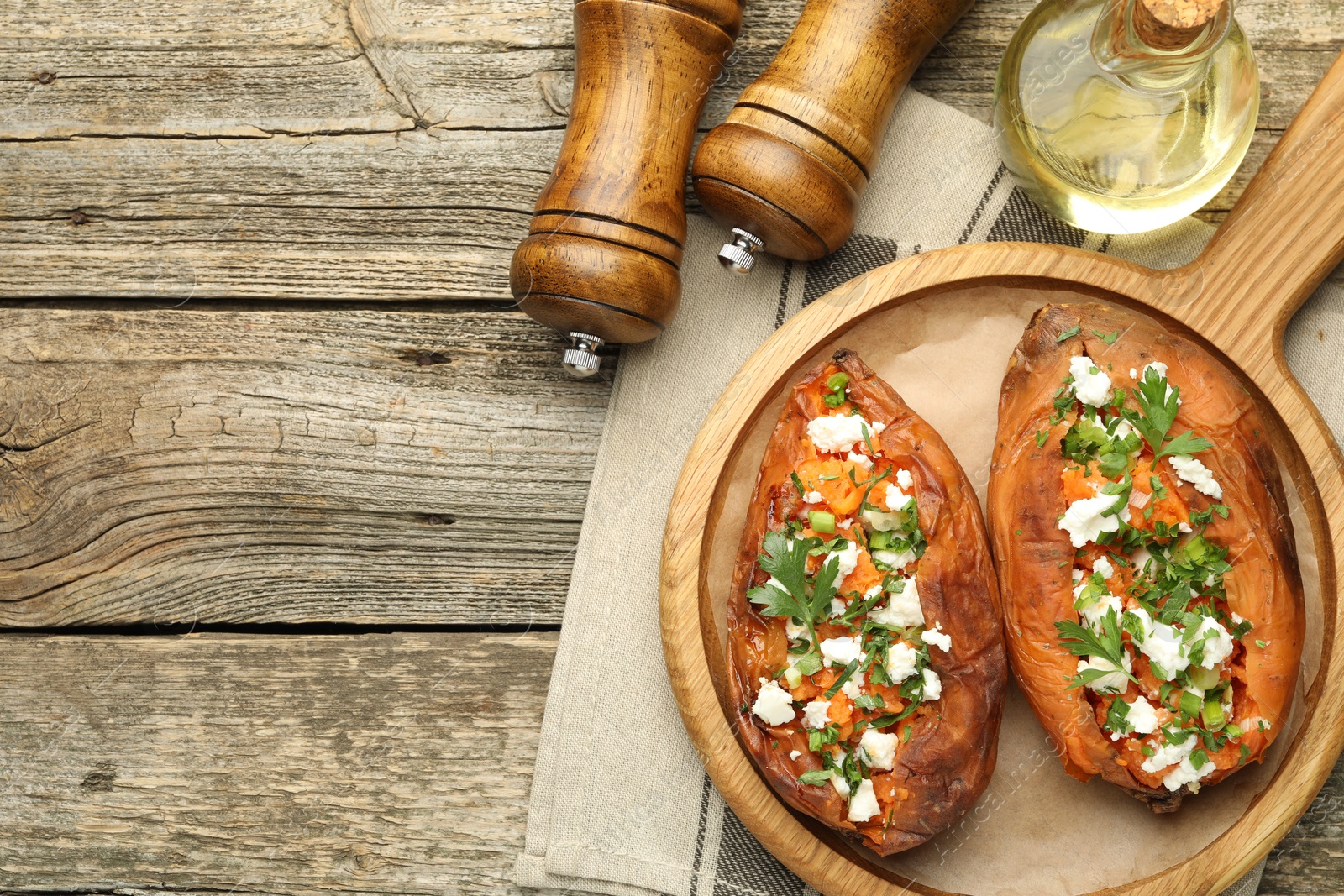 Photo of Tasty cooked sweet potatoes with feta cheese, green onion, parsley and oil on wooden board, flat lay. Space for text