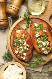 Photo of Tasty cooked sweet potatoes with feta cheese, green onion, parsley and oil on wooden board, flat lay