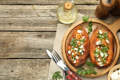 Photo of Tasty cooked sweet potatoes with feta cheese, green onion and parsley served on wooden table, flat lay. Space for text