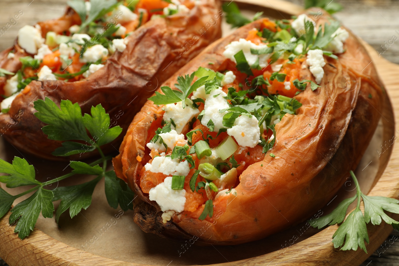 Photo of Tasty cooked sweet potatoes with feta cheese, green onion and parsley on wooden board, closeup