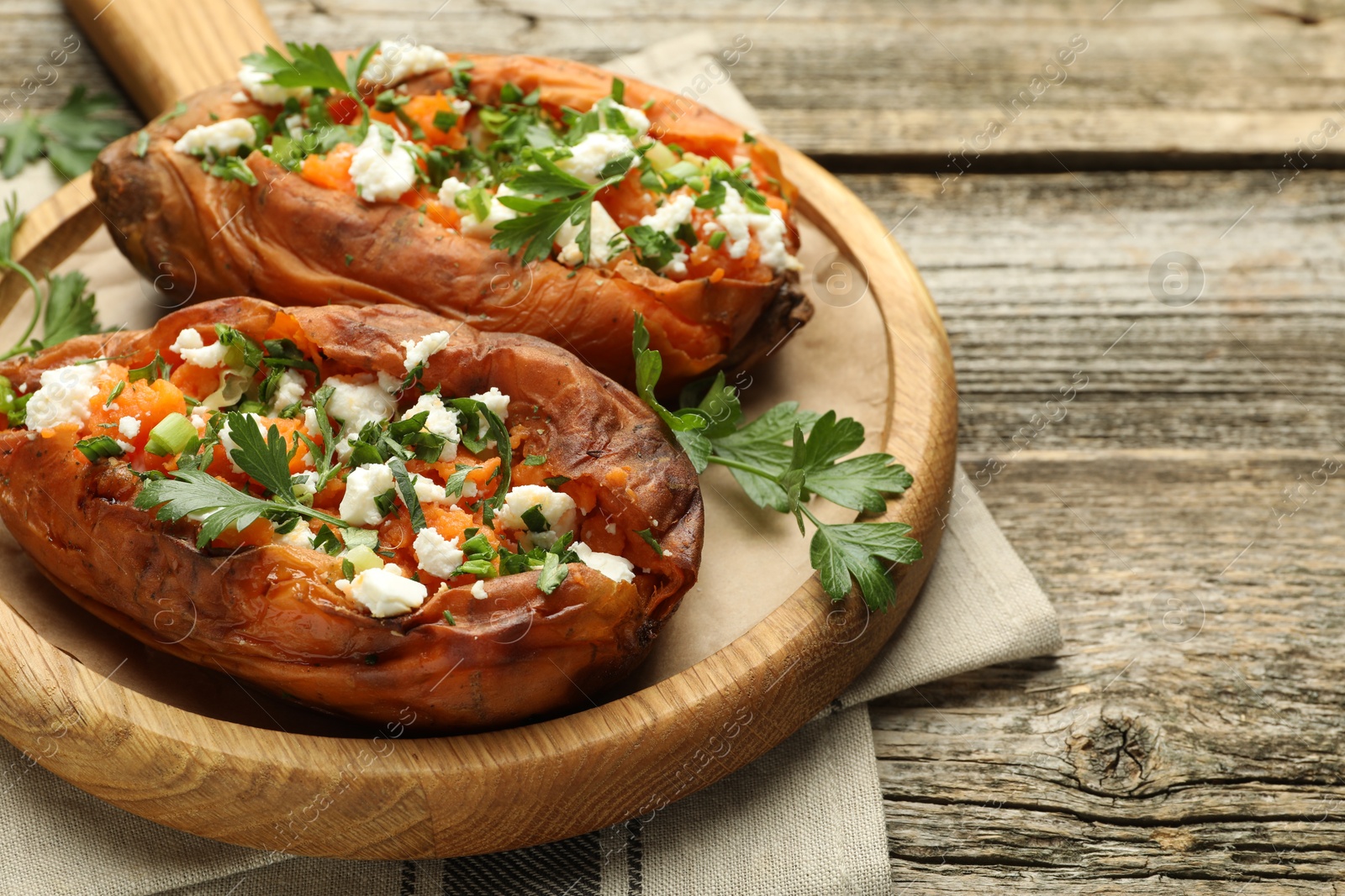 Photo of Tasty cooked sweet potatoes with feta cheese, green onion and parsley on wooden table, closeup