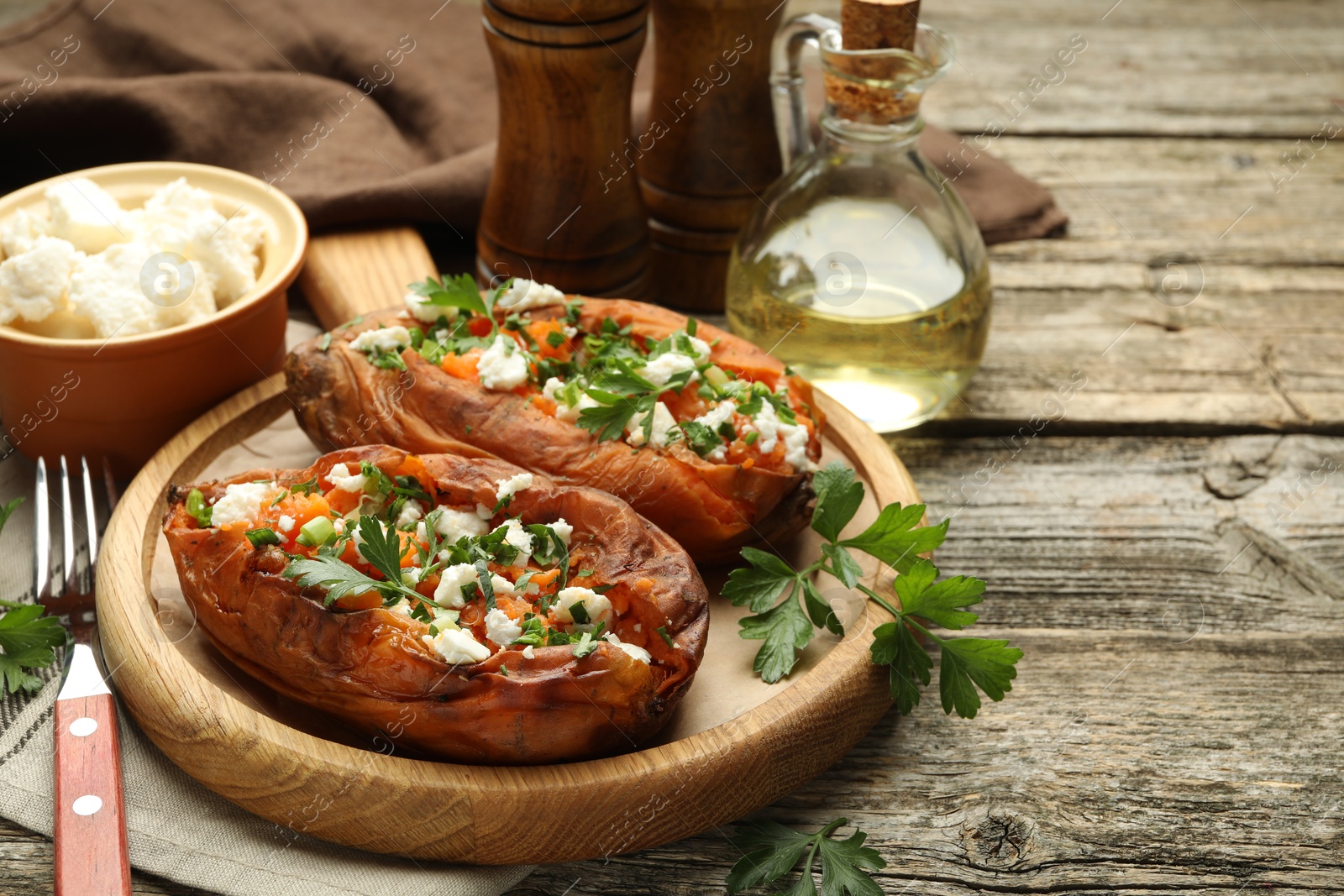 Photo of Tasty cooked sweet potatoes with feta cheese, green onion and parsley served on wooden table, closeup