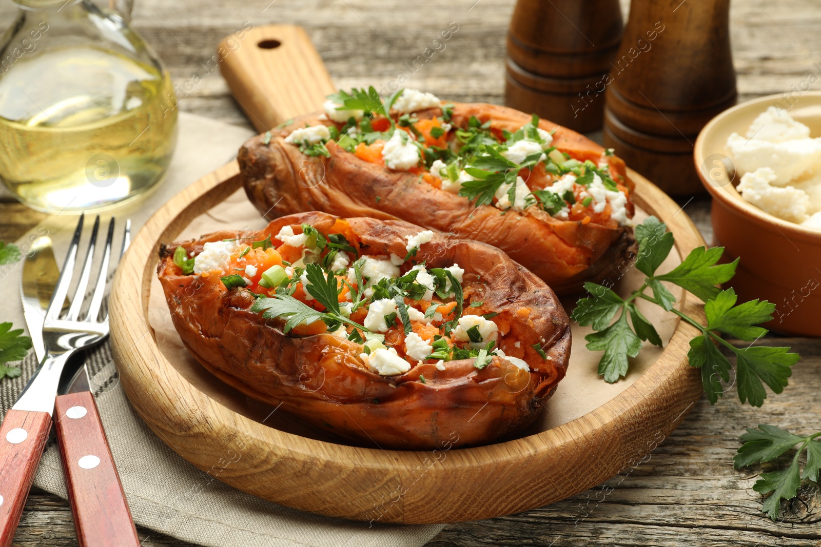 Photo of Tasty cooked sweet potatoes with feta cheese, green onion and parsley served on wooden table, closeup