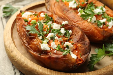 Photo of Tasty cooked sweet potatoes with feta cheese, green onion and parsley on wooden board, closeup