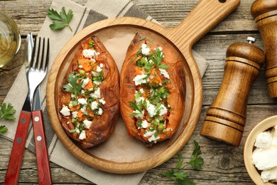 Photo of Tasty cooked sweet potatoes with feta cheese, green onion and parsley served on wooden table, flat lay