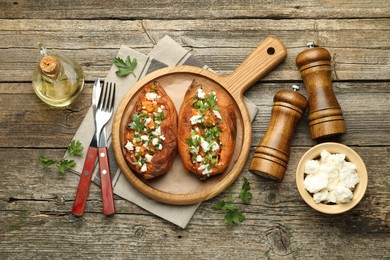 Photo of Tasty cooked sweet potatoes with feta cheese, green onion and parsley served on wooden table, flat lay