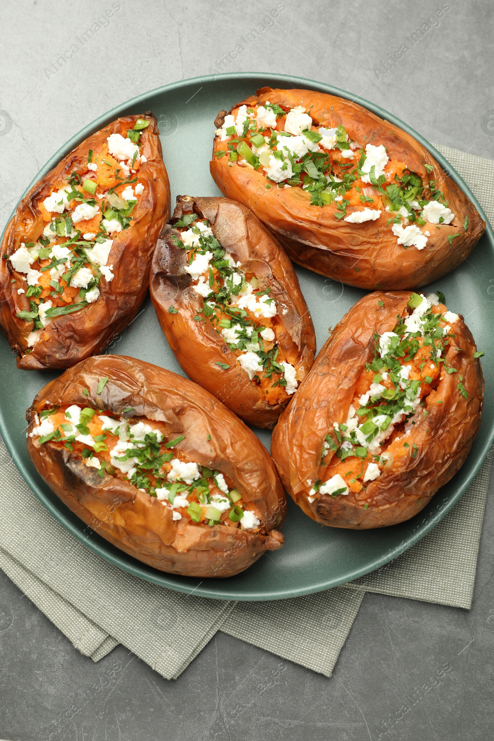 Photo of Tasty cooked sweet potatoes with feta cheese, green onion and parsley on gray textured table, top view