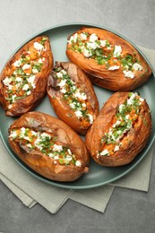 Photo of Tasty cooked sweet potatoes with feta cheese, green onion and parsley on gray textured table, top view