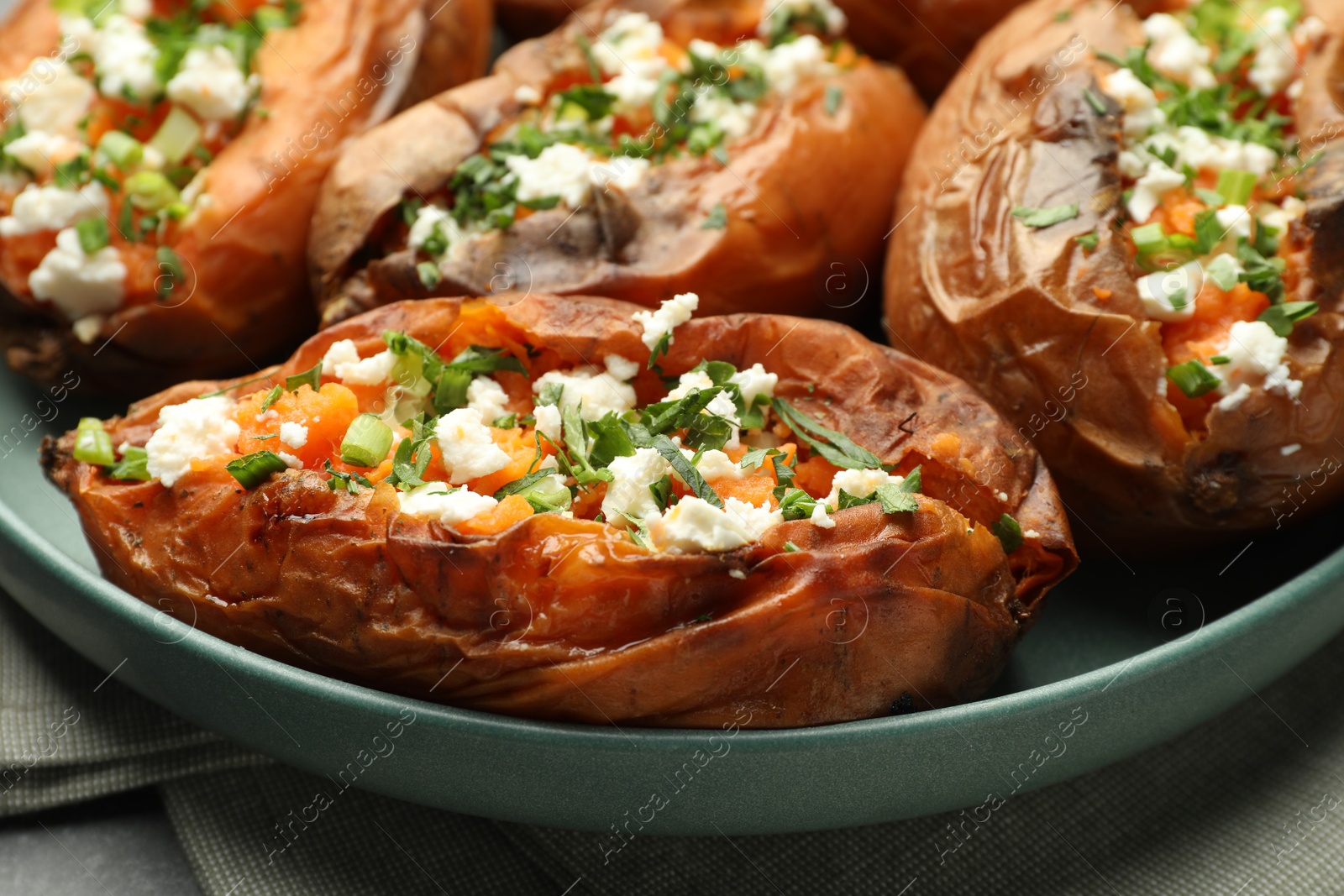 Photo of Tasty cooked sweet potatoes with feta cheese, green onion and parsley on table, closeup