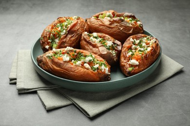 Photo of Tasty cooked sweet potatoes with feta cheese, green onion and parsley on gray textured table, closeup