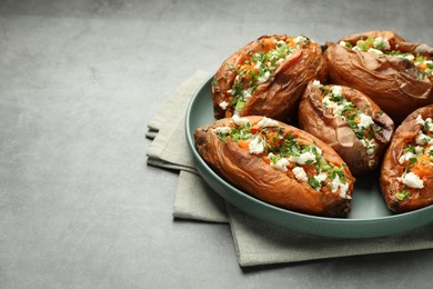 Photo of Tasty cooked sweet potatoes with feta cheese, green onion and parsley on gray textured table, closeup. Space for text