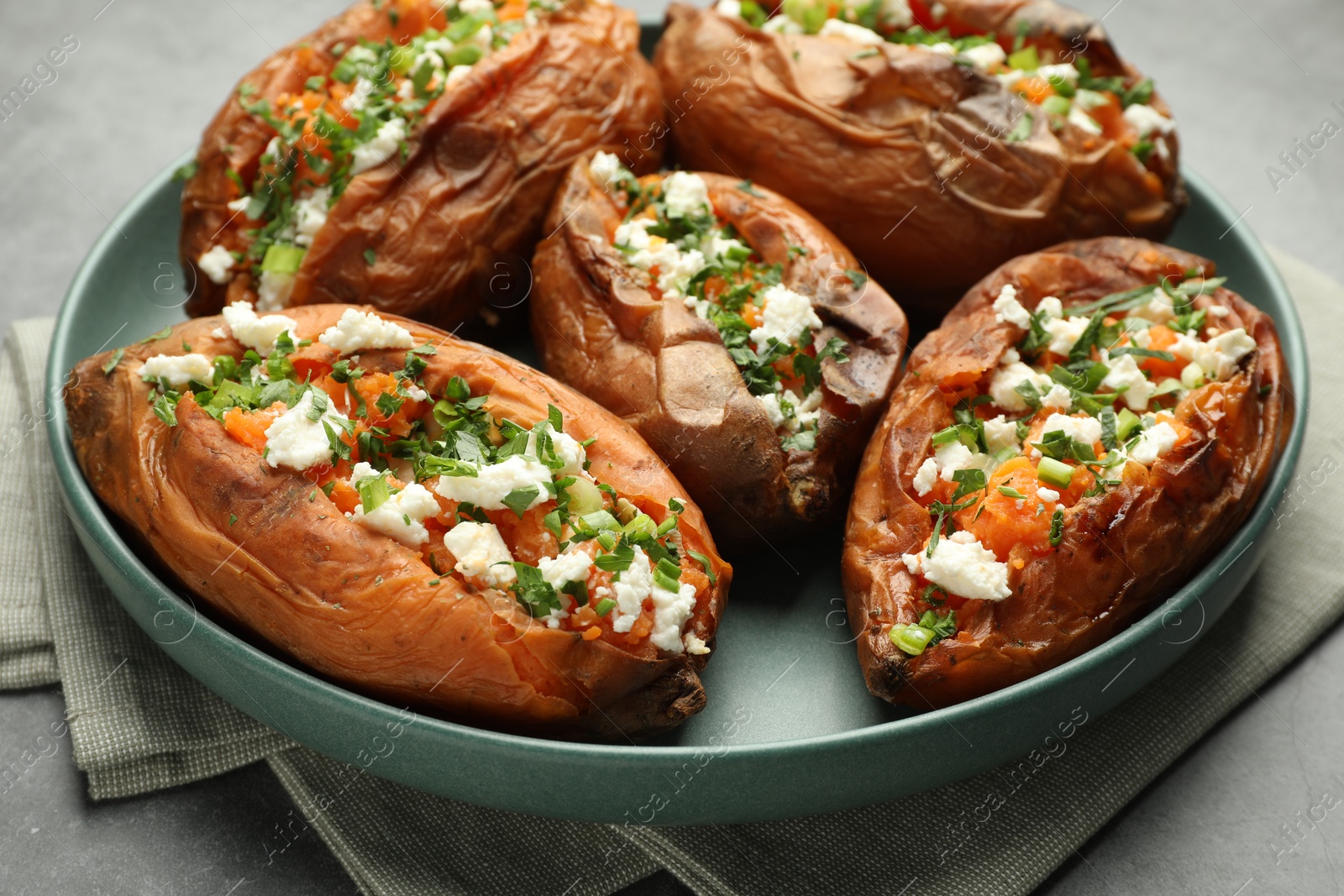 Photo of Tasty cooked sweet potatoes with feta cheese, green onion and parsley on gray table, closeup