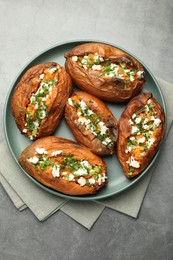 Photo of Tasty cooked sweet potatoes with feta cheese, green onion and parsley on gray textured table, top view