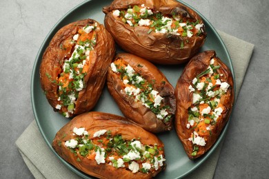 Photo of Tasty cooked sweet potatoes with feta cheese, green onion and parsley on gray textured table, top view