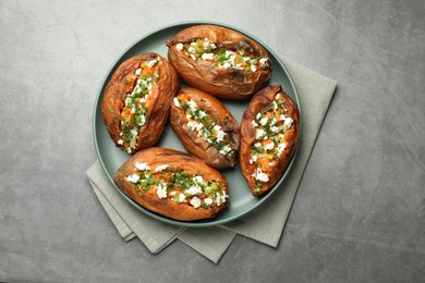 Tasty cooked sweet potatoes with feta cheese, green onion and parsley on gray textured table, top view