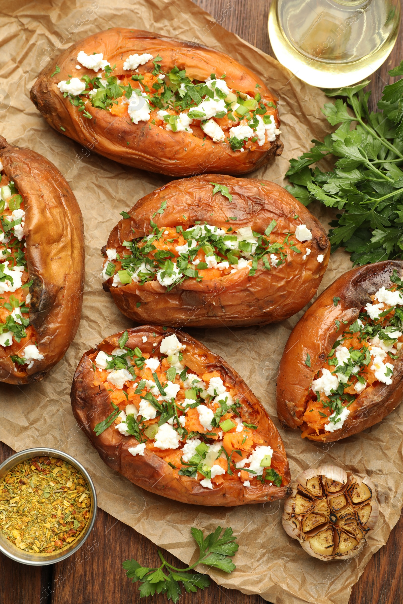 Photo of Tasty cooked sweet potatoes with feta cheese, green onion, spices and oil on wooden table, flat lay