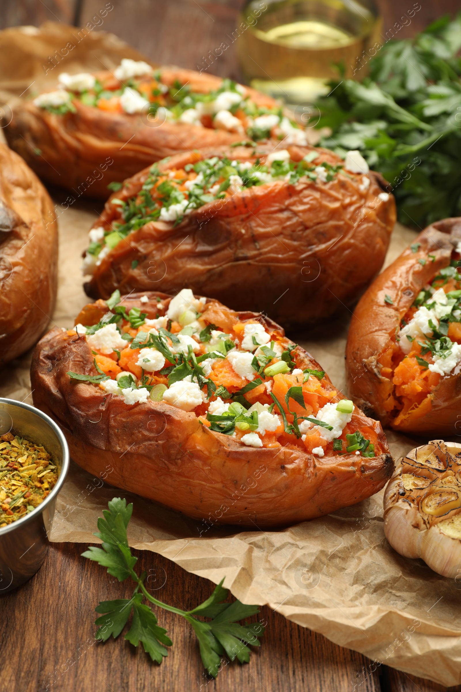 Photo of Tasty cooked sweet potatoes with feta cheese, green onion and parsley on wooden table, closeup