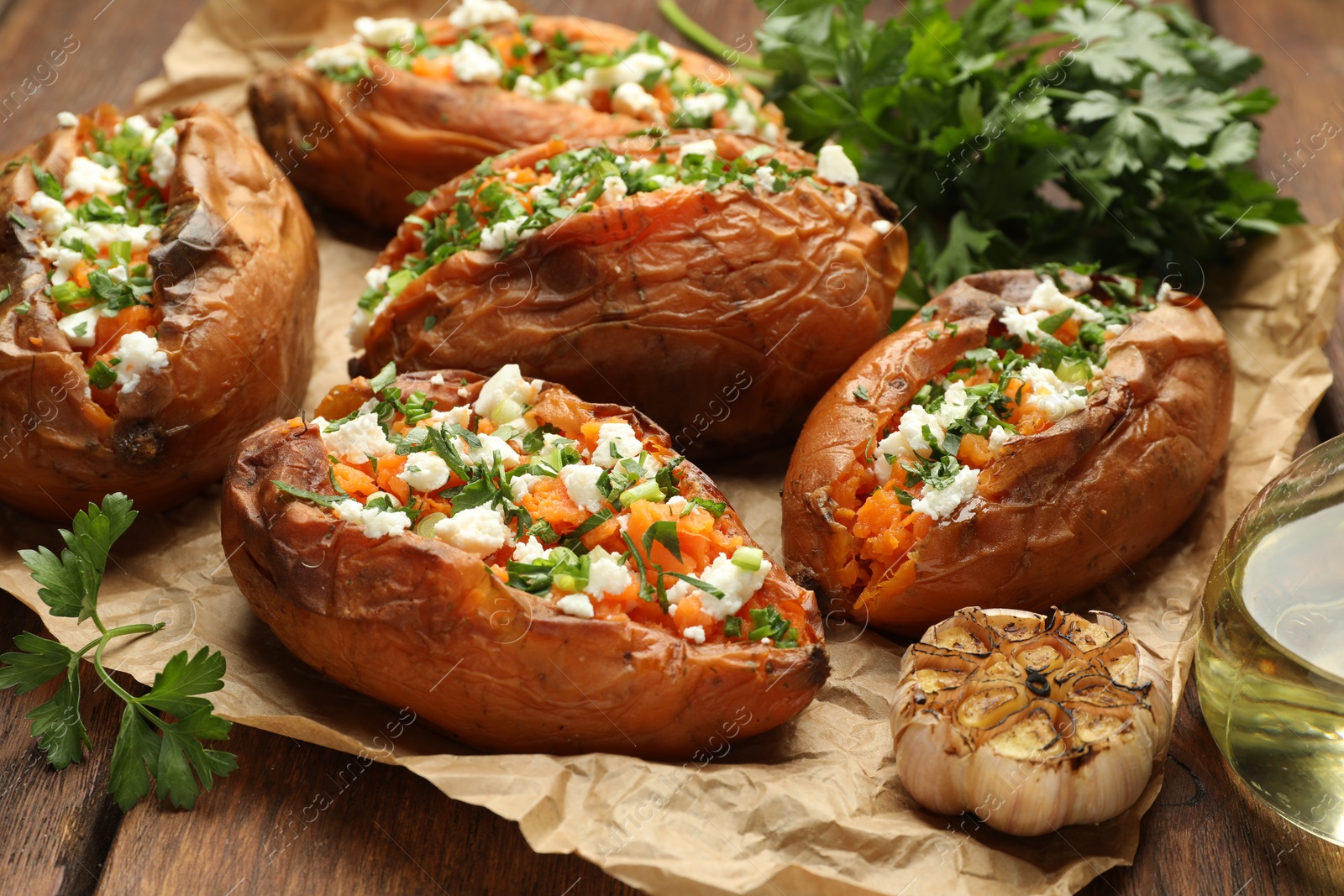 Photo of Tasty cooked sweet potatoes with feta cheese, green onion and parsley on wooden table, closeup