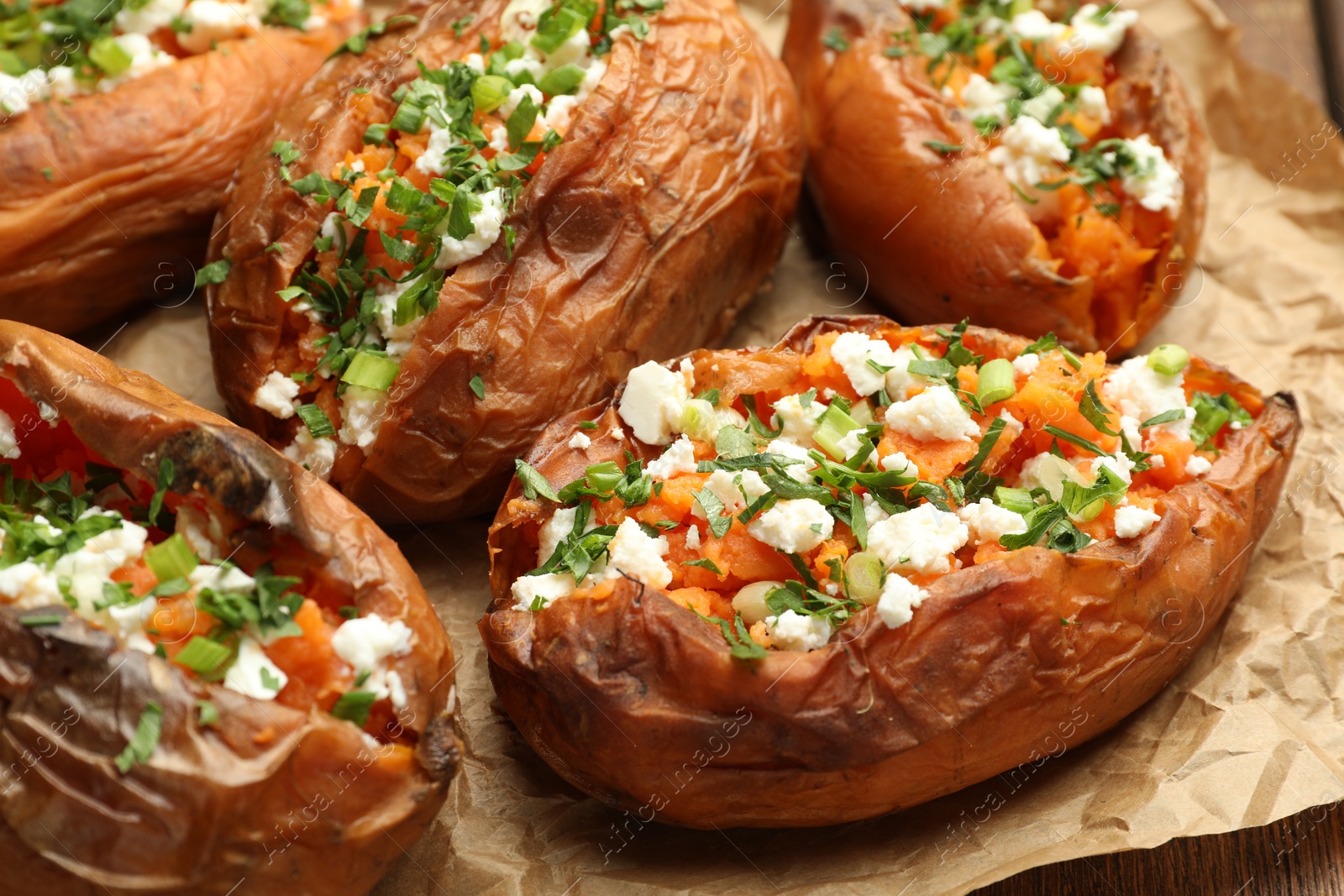 Photo of Tasty cooked sweet potatoes with feta cheese, green onion and parsley on table, closeup