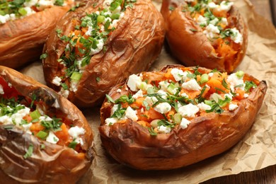 Tasty cooked sweet potatoes with feta cheese, green onion and parsley on table, closeup