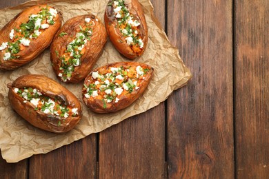 Photo of Tasty cooked sweet potatoes with feta cheese, green onion and parsley on wooden table, top view. Space for text