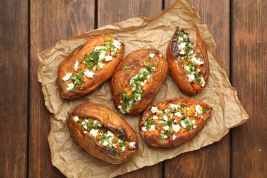 Photo of Tasty cooked sweet potatoes with feta cheese, green onion and parsley on wooden table, top view