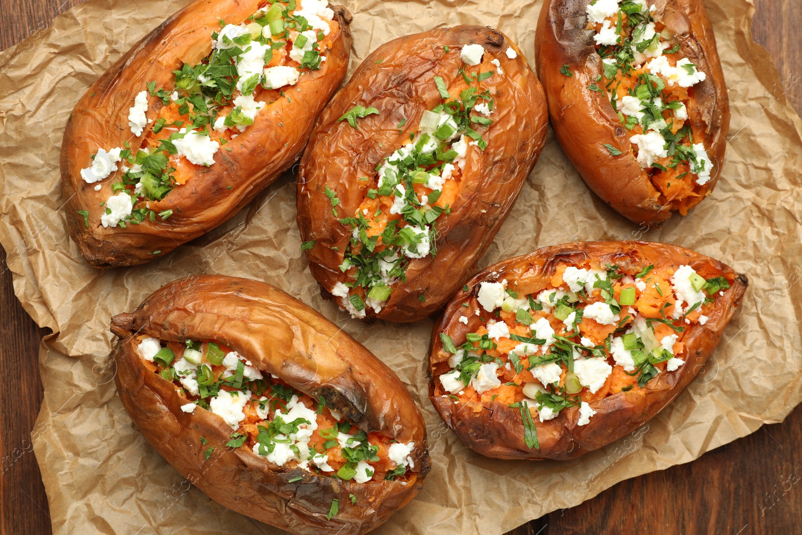 Photo of Tasty cooked sweet potatoes with feta cheese, green onion and parsley on wooden table, top view