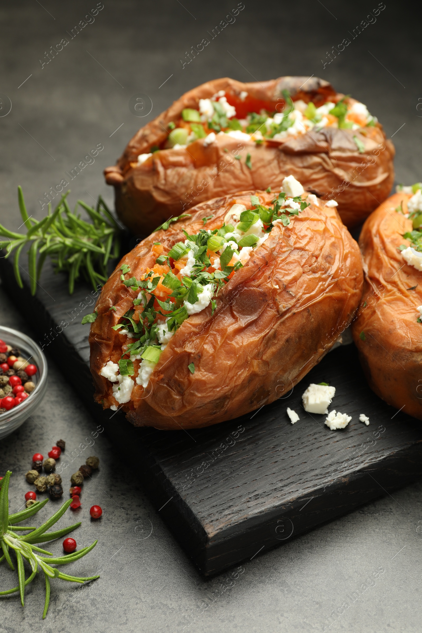 Photo of Tasty cooked sweet potatoes with feta cheese, green onion, parsley and spices on gray textured table, closeup