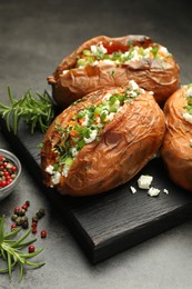 Photo of Tasty cooked sweet potatoes with feta cheese, green onion, parsley and spices on gray textured table, closeup