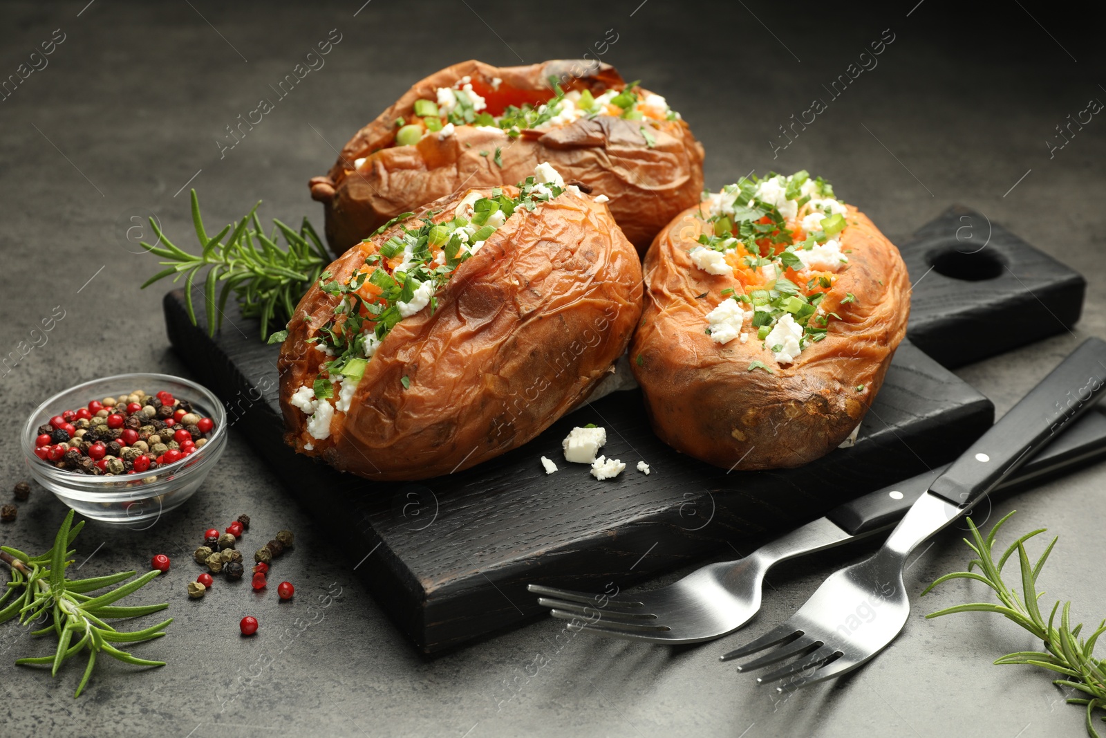 Photo of Tasty cooked sweet potatoes with feta cheese, green onion and parsley served on gray textured table, closeup