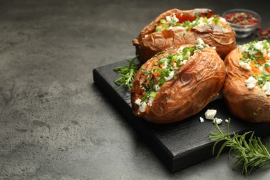 Photo of Tasty cooked sweet potatoes with feta cheese, green onion, parsley and rosemary on gray textured table, closeup. Space for text