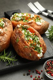 Tasty cooked sweet potatoes with feta cheese, green onion, parsley and spices on gray textured table, closeup