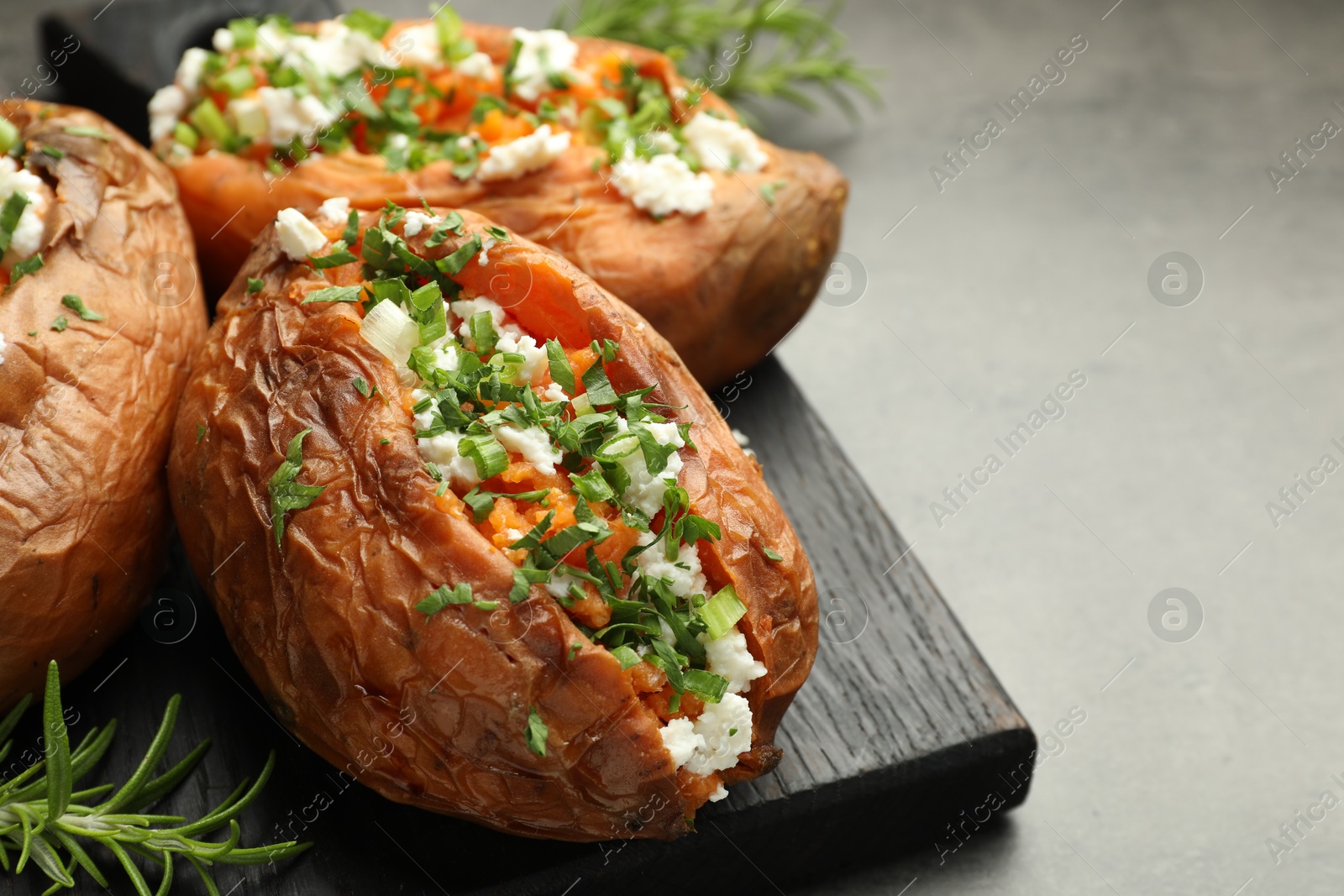 Photo of Tasty cooked sweet potatoes with feta cheese, green onion, parsley and rosemary on gray table, closeup. Space for text