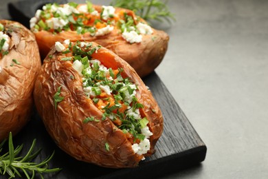 Tasty cooked sweet potatoes with feta cheese, green onion, parsley and rosemary on gray table, closeup. Space for text