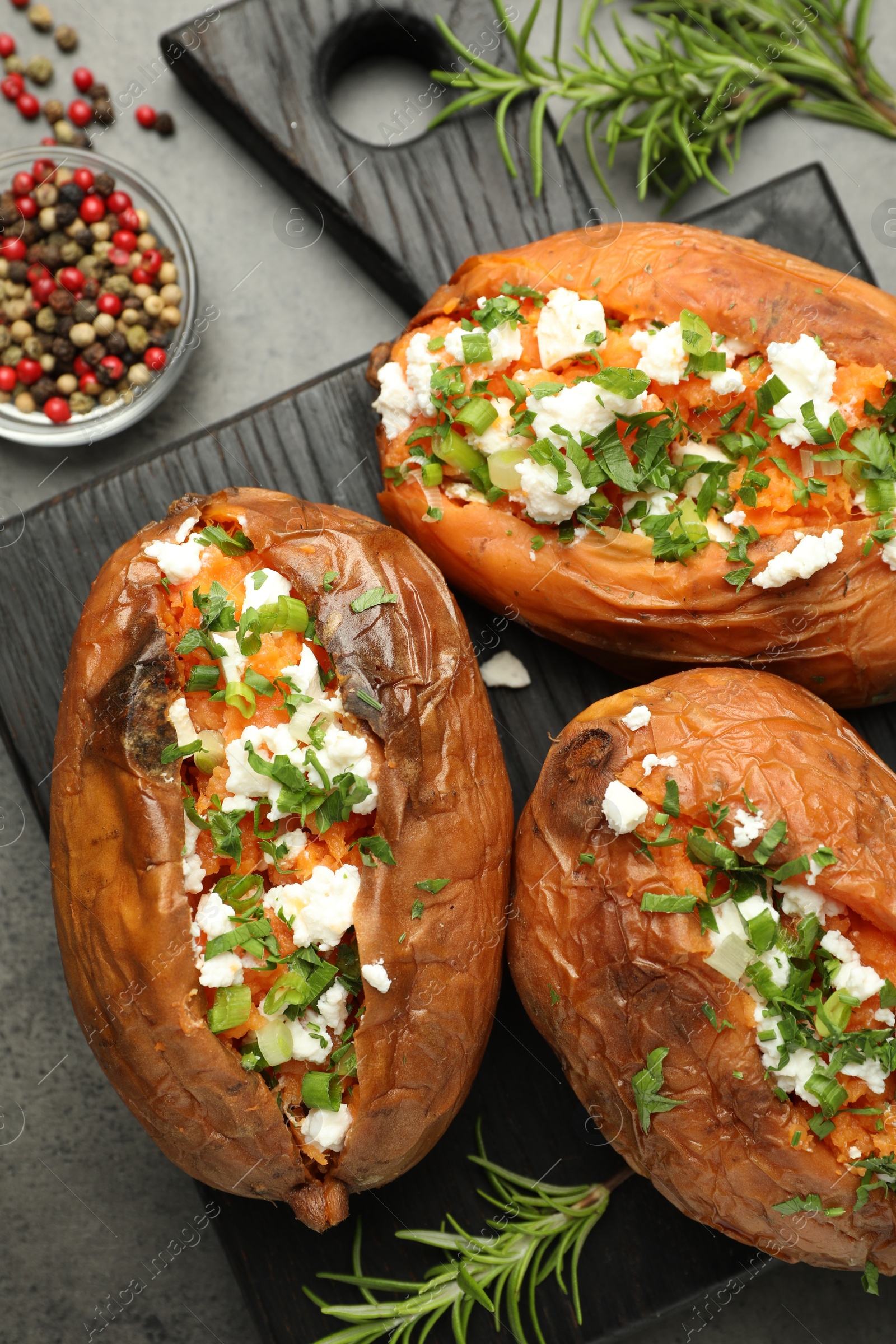 Photo of Tasty cooked sweet potatoes with feta cheese, green onion, parsley and spices on gray textured table, flat lay