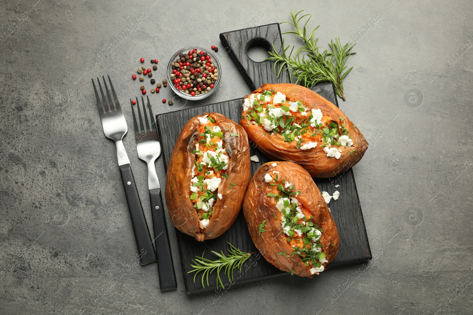 Photo of Tasty cooked sweet potatoes with feta cheese, green onion and parsley served on gray textured table, flat lay