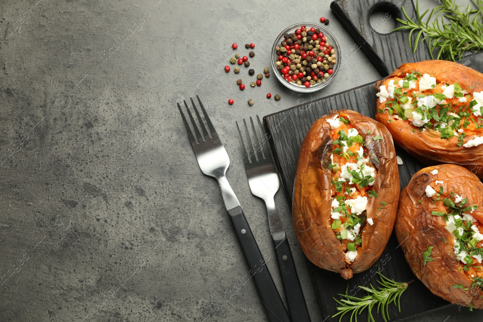 Photo of Tasty cooked sweet potatoes with feta cheese, green onion and parsley served on gray textured table, flat lay. Space for text