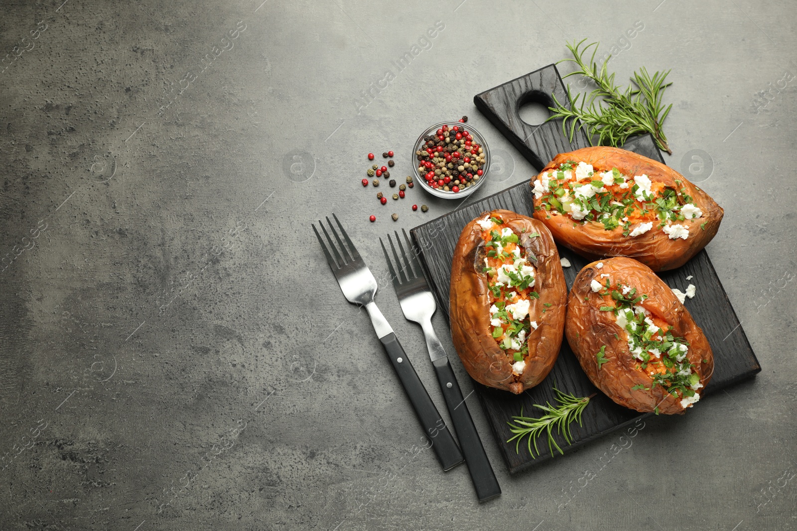 Photo of Tasty cooked sweet potatoes with feta cheese, green onion and parsley served on gray textured table, flat lay. Space for text