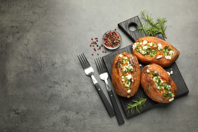 Tasty cooked sweet potatoes with feta cheese, green onion and parsley served on gray textured table, flat lay. Space for text