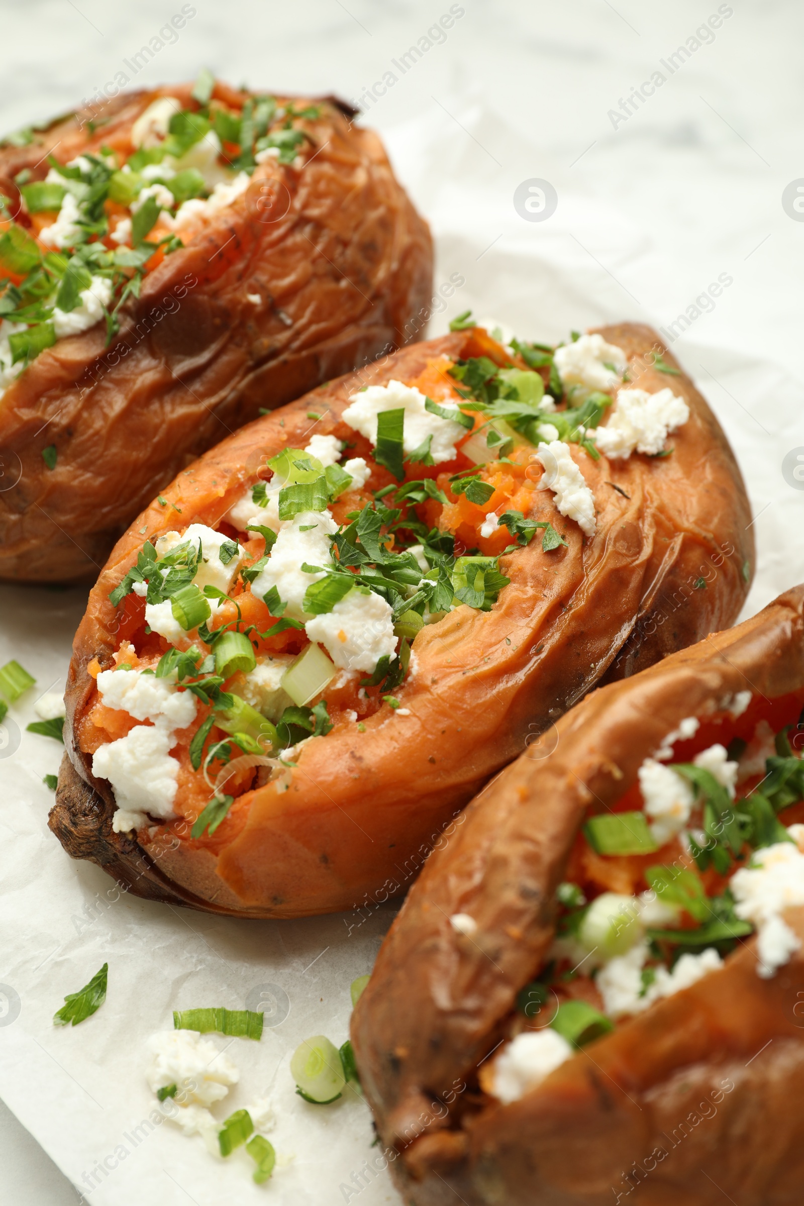 Photo of Tasty cooked sweet potatoes with feta cheese, green onion and parsley on table, closeup