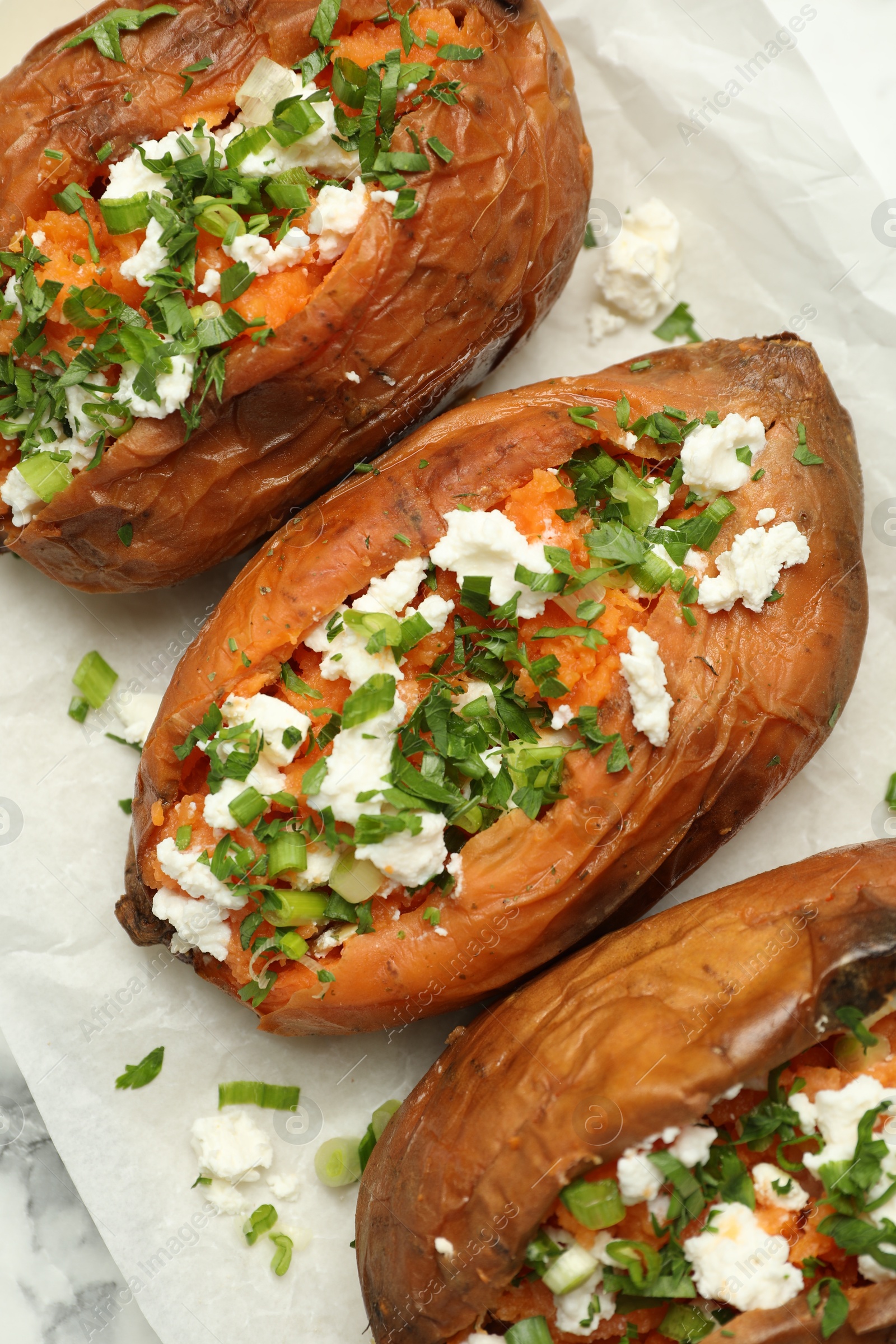 Photo of Tasty cooked sweet potatoes with feta cheese, green onion and parsley on white table, top view