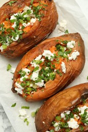 Photo of Tasty cooked sweet potatoes with feta cheese, green onion and parsley on white table, top view