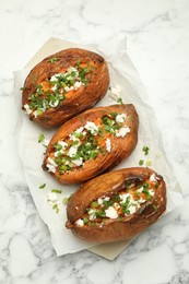 Photo of Tasty cooked sweet potatoes with feta cheese, green onion and parsley on white marble table, top view