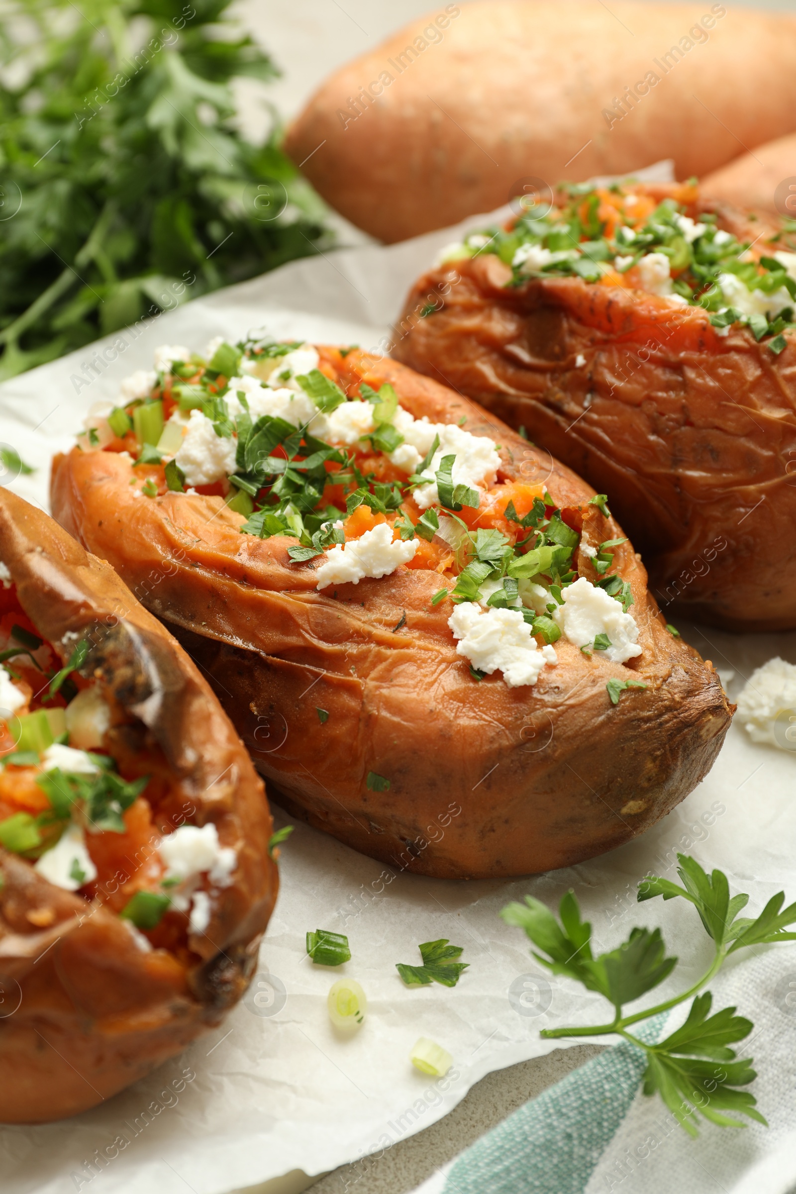 Photo of Tasty cooked sweet potatoes with feta cheese, green onion and parsley on table, closeup