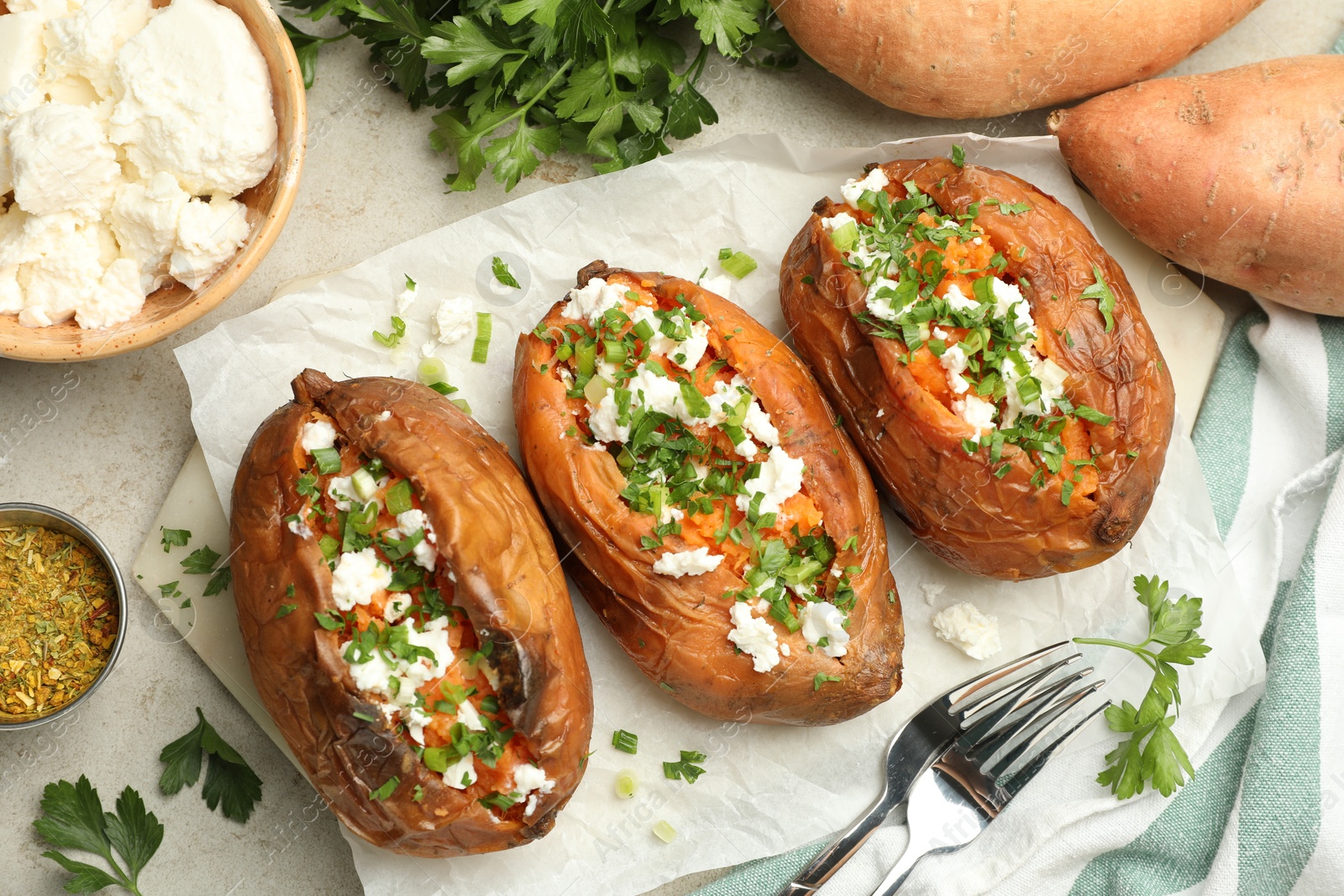 Photo of Tasty cooked sweet potatoes with feta cheese, green onion and parsley served on gray textured table, flat lay