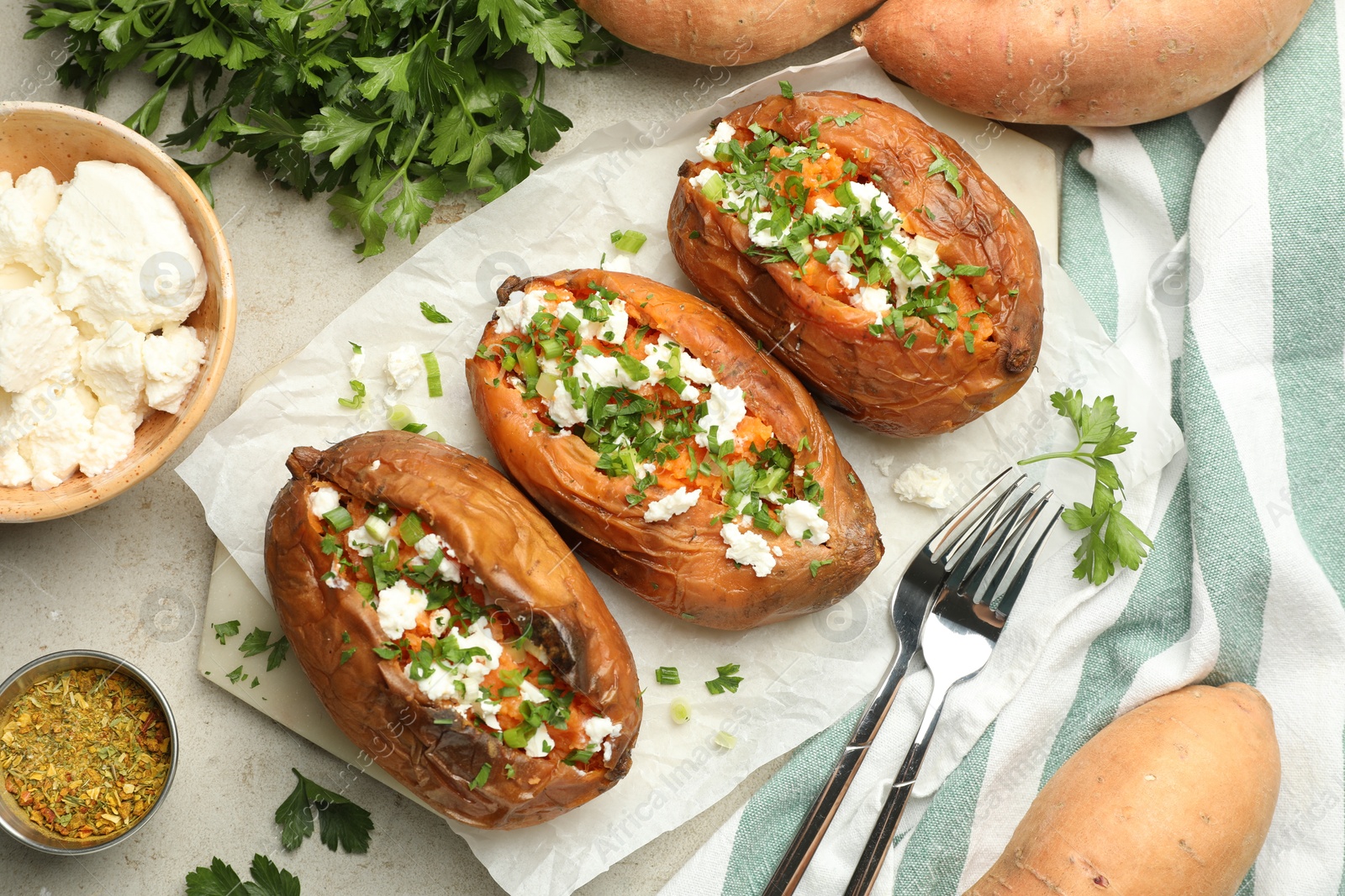 Photo of Tasty cooked sweet potatoes with feta cheese, green onion and parsley served on gray textured table, flat lay