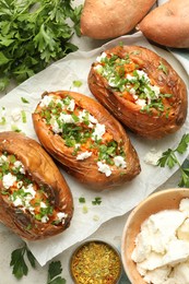 Photo of Tasty cooked sweet potatoes with feta cheese, green onion and parsley on table, flat lay