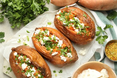 Tasty cooked sweet potatoes with feta cheese, green onion and parsley on table, flat lay