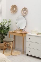 Photo of Mirror, dressing table, houseplant, stool and chest of drawers indoors. Interior design